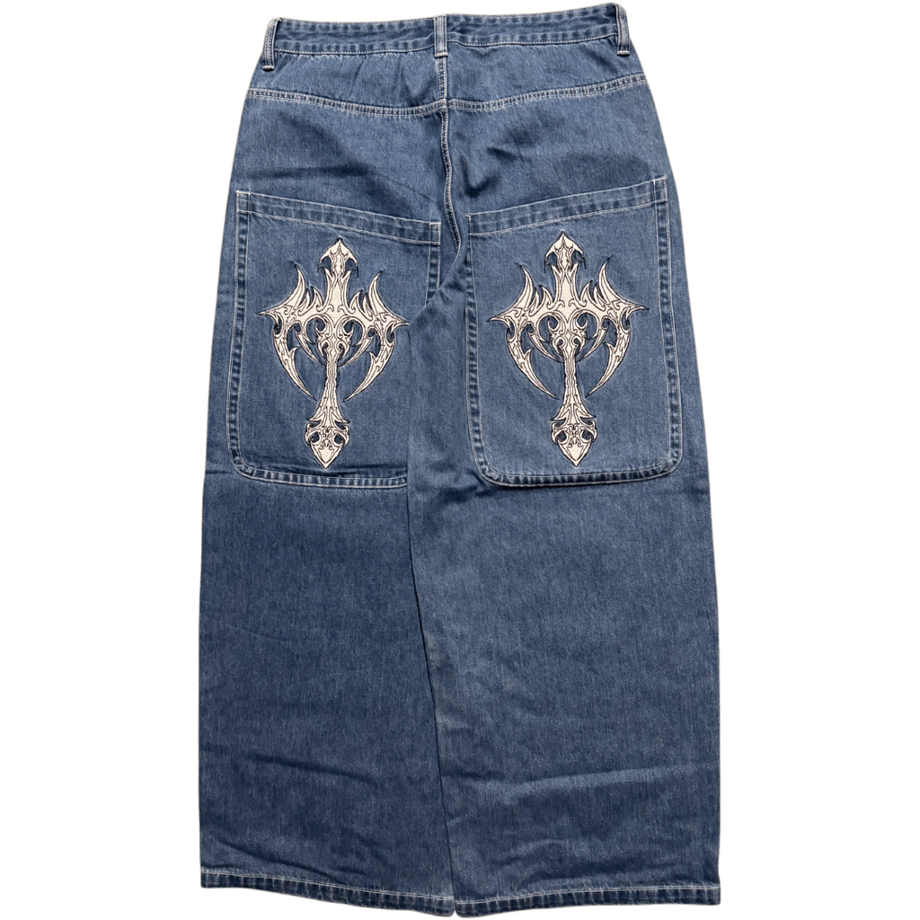 A blue denim skirt shown from the back, featuring two large patch pockets with ornate silver metallic cross embroidery on each pocket.