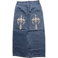 A blue denim skirt shown from the back, featuring two large patch pockets with ornate silver metallic cross embroidery on each pocket.
