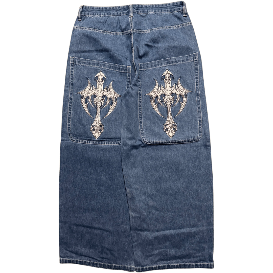 A blue denim skirt shown from the back, featuring two large patch pockets with ornate silver metallic cross embroidery on each pocket.